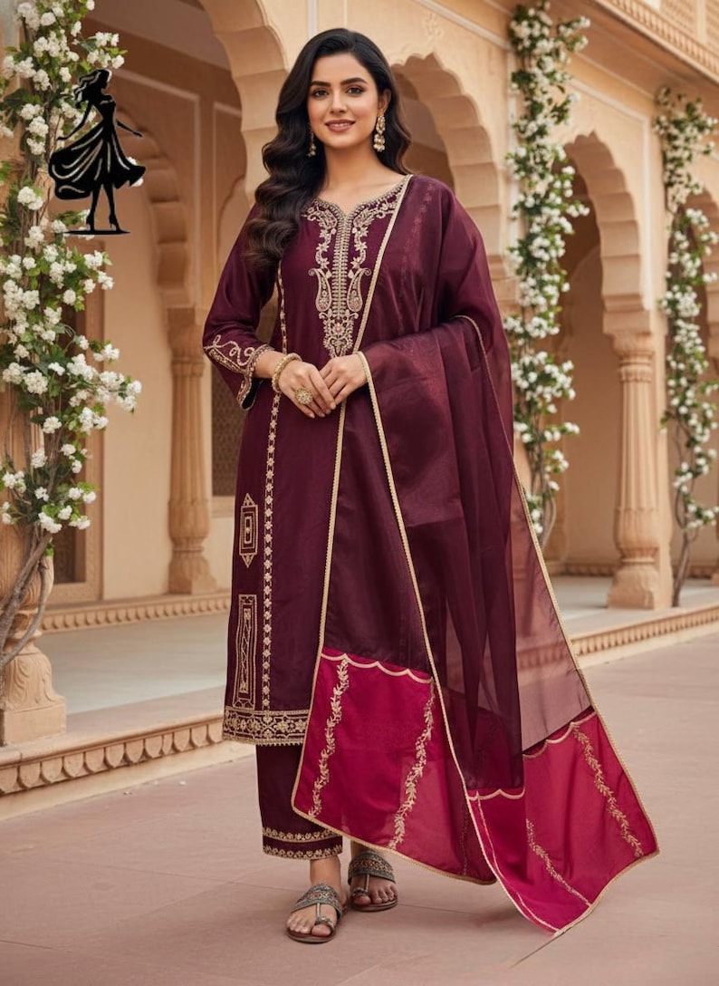 Puede incluir: Un conjunto de salwar kameez burdeos con bordados dorados. El atuendo incluye una t&uacute;nica de manga larga, pantalones a juego y una dupatta transparente. El dise&ntilde;o presenta intrincados patrones dorados en el escote, las mangas y el dobladillo.