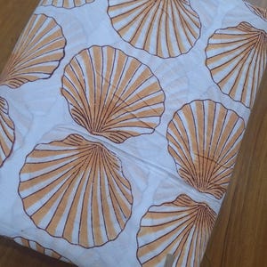 Könnte beinhalten: Weißer Stoff mit einem sich wiederholenden Muster aus großen, orangefarbenen und braunen Muscheln. Das Muscheldesign ist mit radialen Linien detailliert. Der Stoff ist gefaltet und zeigt mehrere Schichten. Geeignet für Heimdekoration oder Kleidung.