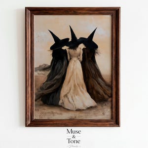 May include: A framed wall art print depicting three figures wearing pointed black hats and long flowing dresses in black, cream, and brown. The figures stand together in a desert landscape under a pale sky. The text Muse & Tone Prints is below.