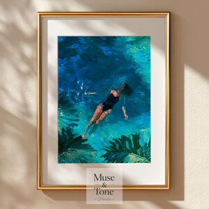 May include: A framed art print featuring a painting of a person in a black swimsuit floating in vibrant blue water, surrounded by large green tropical leaves. The print includes the text Muse & Tone Prints at the bottom center of the white mat.