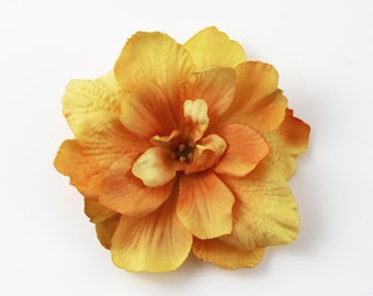 May include: A single, large, orange and yellow artificial flower with multiple petals. The flower is made of fabric and has a realistic appearance.
