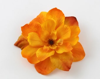 May include: A vibrant, artificial flower in shades of orange and yellow. The flower has multiple layers of petals, with a darker center. The petals transition from a bright yellow to a deep orange, creating a gradient effect. The flower is likely for decorative purposes.