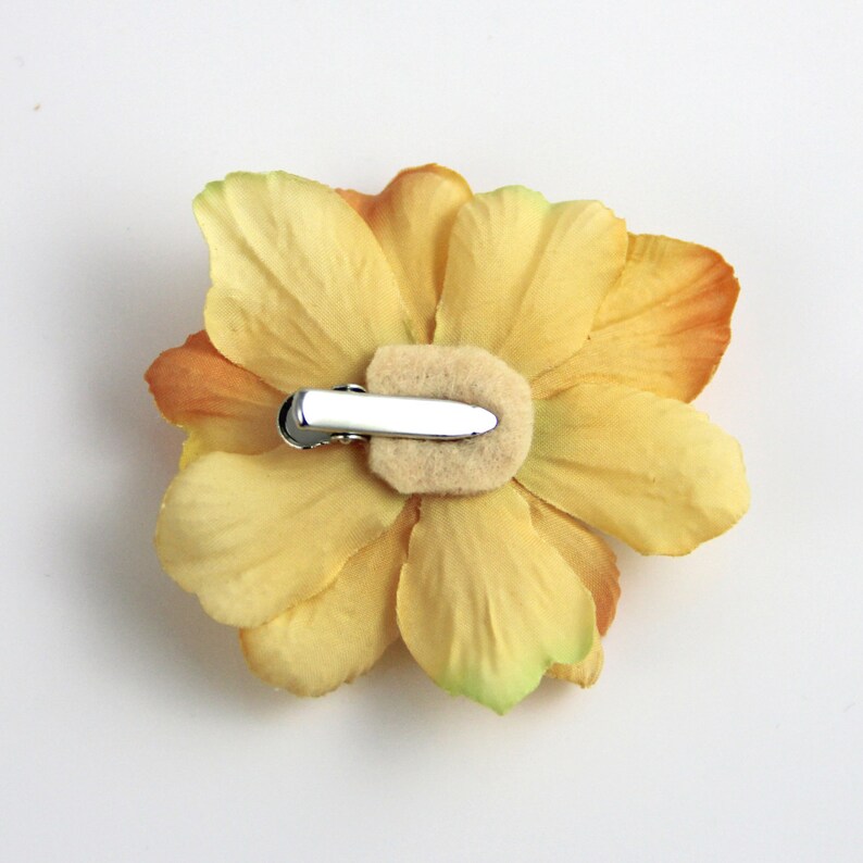 May include: A yellow flower hair clip with a brown center. The clip is attached to the back of the flower.
