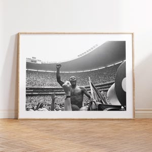 Könnte beinhalten: Schwarz-Weiß-Druck in einem Rahmen, der einen jubelnden Mann mit erhobener Faust in einem Stadion zeigt, umgeben von einer jubelnden Menge. Das Bild fängt einen Moment des Triumphs ein, mit dem Fokus auf dem Gesichtsausdruck der Hauptfigur.