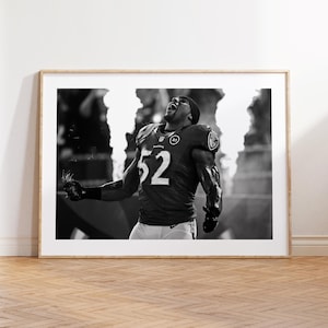 Könnte beinhalten: Schwarz-Weiß-Druck in einem Rahmen eines Footballspielers in einem lila Trikot mit der Nummer 52. Der Spieler jubelt mit erhobenen Armen, Flammen im Hintergrund. Das Bild wird in einem Holzrahmen präsentiert.