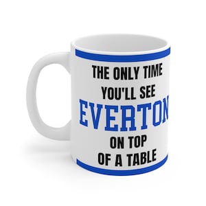 Puede incluir: Taza de cerámica blanca con borde y asa azules. La taza presenta el texto "THE ONLY TIME YOU'LL SEE EVERTON ON TOP OF A TABLE" en letras negras y azules. Un regalo humorístico.