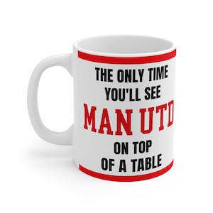 May include: White ceramic mug with a red trim and handle. The mug features the text "THE ONLY TIME YOU'LL SEE MAN UTD ON TOP OF A TABLE" in black and red.