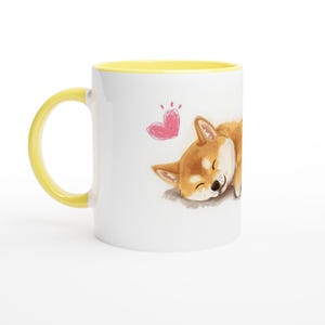 以下が含まれることがあります： 黄色い内側とハンドルが付いた白いセラミックマグ。マグカップには、ピンクのハートが上に描かれた、眠っている柴犬の犬の水彩イラストが描かれています。犬は茶色と白です。
