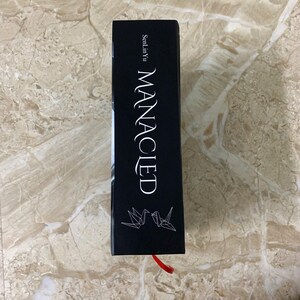 K&ouml;nnte beinhalten: Ein schwarzes Buch mit dem Titel "MANACIED" in wei&szlig;er Schrift. Der Name des Autors, SenLinYu, ist &uuml;ber dem Titel aufgedruckt. Zwei Origami-V&ouml;gel befinden sich am unteren Rand. Ein rotes Leseb&auml;ndchen ist sichtbar.