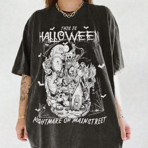 Puede incluir: Camiseta negra con un dise&ntilde;o gr&aacute;fico en blanco y negro inspirado en "Pesadilla antes de Navidad". El dise&ntilde;o incluye el texto "THIS IS HALLOWEEN" y "NIGHTMARE ON MAIN STREET", con murci&eacute;lagos y telara&ntilde;as.