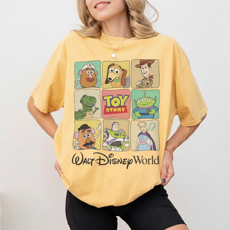 May include: Yellow t-shirt featuring a grid of Toy Story characters, including Mr. Potato Head, Woody, and Buzz Lightyear. The shirt also has the text "Toy Story" and "Walt Disney World" printed on it.