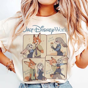 May include: A cream-coloured sweatshirt with a Walt Disney World logo and a four-panel illustration of Zootopia characters. The panels show Nick Wilde and Judy Hopps in romantic poses, with text including "Sweet Surrender" and "Adventure Awaits".