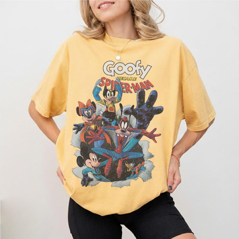 Op de afbeelding: Mosterdgeel T-shirt met een afbeelding van Disney-figuren in superhelden kostuums, waaronder Goofy als Spider-Man. De tekst "Goofy Became Spider-Man" staat boven de figuren. Het shirt heeft een vintage, distressed look.