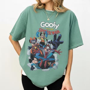 Op de afbeelding: Groen t-shirt met een afbeelding van Goofy als Spider-Man en andere Disney-personages. De tekst "Goofy became Spider-Man" staat boven de personages. Het shirt heeft korte mouwen en een ronde hals.