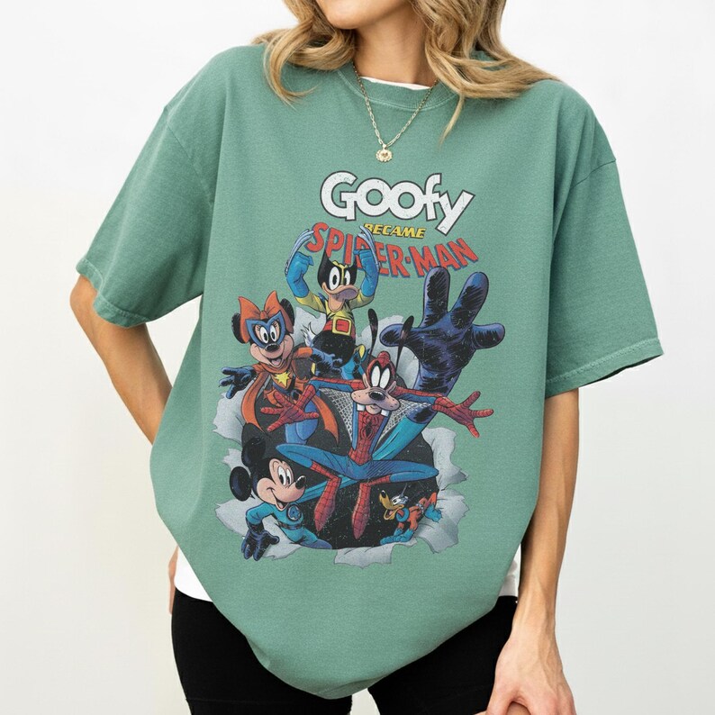 Op de afbeelding: Groen t-shirt met een afbeelding van Goofy als Spider-Man en andere Disney-personages. De tekst "Goofy became Spider-Man" staat boven de personages. Het shirt heeft korte mouwen en een ronde hals.