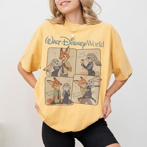 May include: Mustard yellow t-shirt with a Zootropolis graphic. The design shows Nick Wilde and Judy Hopps in four panels, with "Walt Disney World" above. The tee shirt is made of a soft material and is suitable for casual wear.