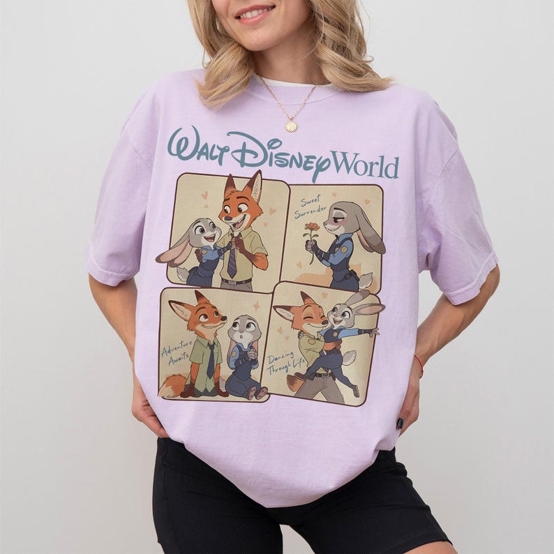 May include: A lilac t-shirt with a four-panel graphic of Zootopia characters. The top panel reads "Walt Disney World". The graphic depicts Nick Wilde and Judy Hopps in various poses. The shirt is made of a soft material.