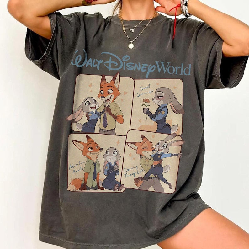 May include: A dark grey t-shirt with a four-panel illustration of Zootopia characters. The top panel reads "Walt Disney World" in blue. Each panel depicts Nick Wilde and Judy Hopps in various poses, with phrases like "Sweet Surrender" and "Adventure Awaits".