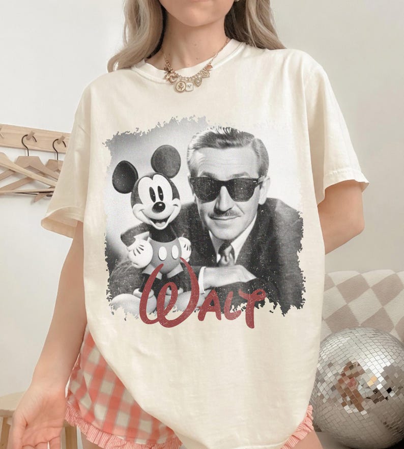K&ouml;nnte beinhalten: Cremefarbenes T-Shirt mit einem Schwarz-Wei&szlig;-Bild von Mickey Mouse und Walt Disney. Das Wort "WALT" ist in roter Schrift darunter geschrieben. Das Shirt hat kurze &Auml;rmel und eine lockere Passform.