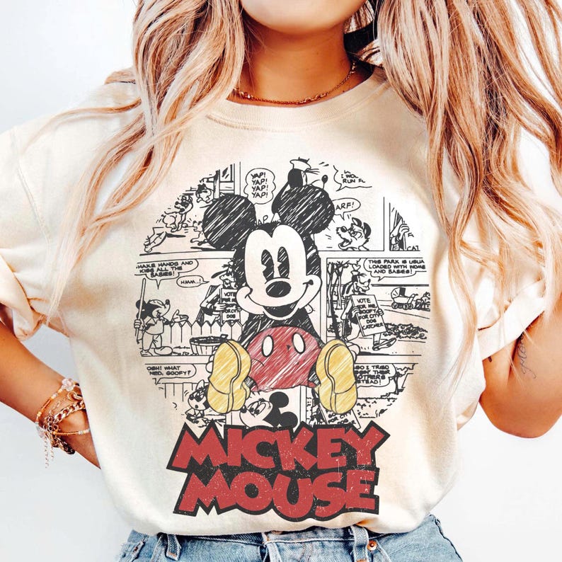 May include: Cream-colored sweatshirt featuring a Mickey Mouse graphic. The graphic includes a circular comic strip design with Mickey Mouse in the center, wearing red shorts and yellow shoes. The words "MICKEY MOUSE" are in red block letters at the bottom.