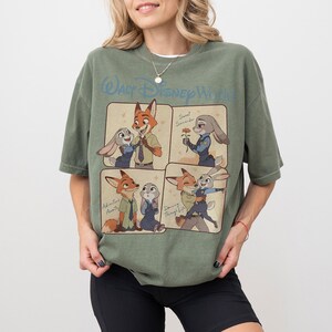 May include: An olive green t-shirt with a four-panel cartoon design featuring Zootopia characters. The shirt has the text "Walt Disney World" across the top. The cartoon panels show the characters in different poses.