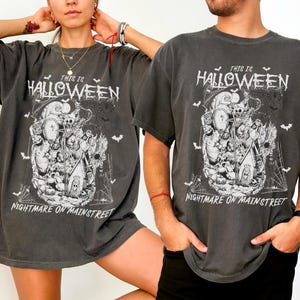 Puede incluir: Camisetas grises oscuras con un dise&ntilde;o de Halloween. El dise&ntilde;o presenta calaveras, murci&eacute;lagos y las frases "This is Halloween" y "Nightmare on Mainstreet" en letras blancas. Las camisetas tienen mangas cortas y un corte holgado.