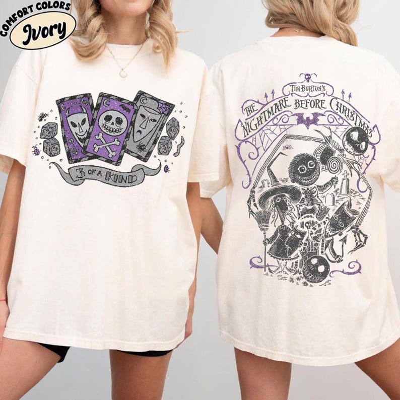 May include: Ivory-colored t-shirt featuring a graphic from "The Nightmare Before Christmas." The front displays three playing cards with character faces and the text "3 of a Kind." The back has a large illustration with the film's title and characters.