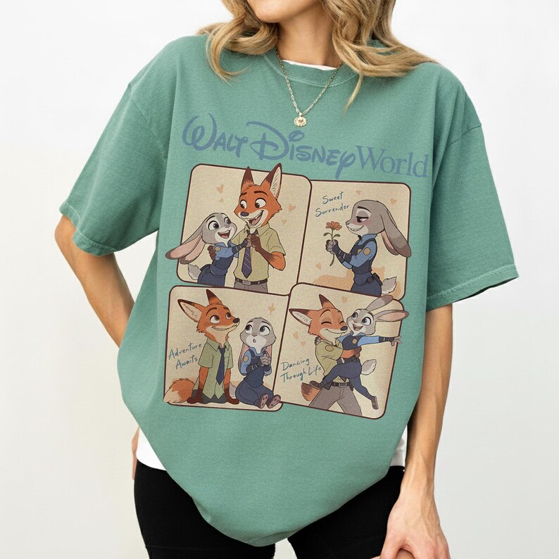 May include: A green t-shirt with a Walt Disney World design. The shirt displays four panels with illustrations of Zootopia characters Nick Wilde and Judy Hopps. Text includes "Adventure Awaits", "Sweet Surrender", and "Dancing Through Life".
