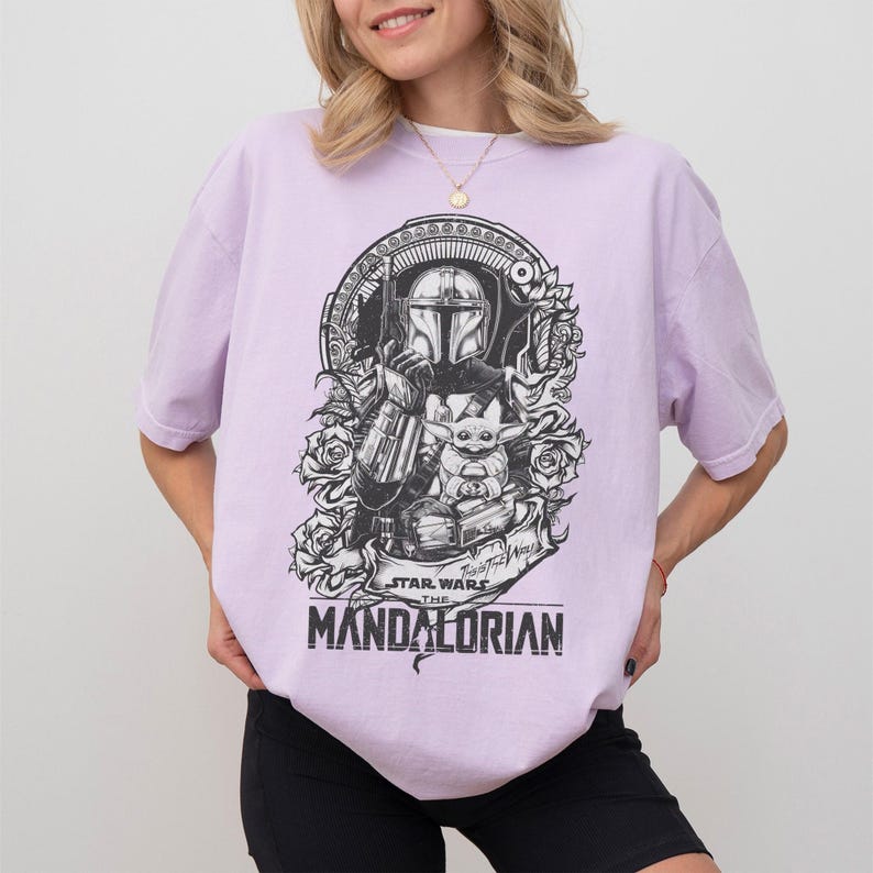 May include: A light purple t-shirt featuring a black and white graphic of The Mandalorian and Grogu from Star Wars. The design includes roses and the text "STAR WARS THE MANDALORIAN".