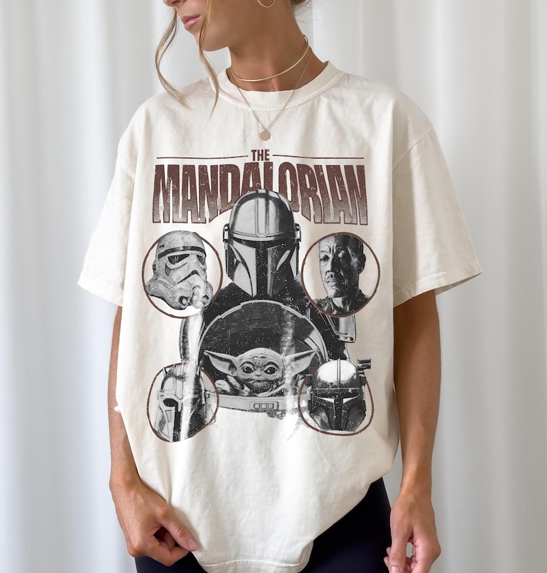 Pu&ograve; includere: T-shirt color crema con la scritta "The Mandalorian" in un carattere marrone invecchiato. La grafica include immagini dei personaggi dello show, tra cui il Mandaloriano, uno Stormtrooper e Grogu. Una maglietta a tema Star Wars.