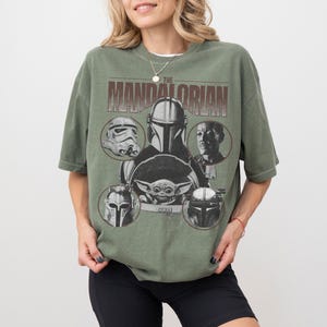 Pu&ograve; includere: T-shirt verde oliva con grafica di "The Mandalorian". Il design include il titolo dello show e immagini di personaggi come il Mandaloriano, Grogu e Stormtroopers. La maglietta ha maniche corte e una vestibilit&agrave; ampia.