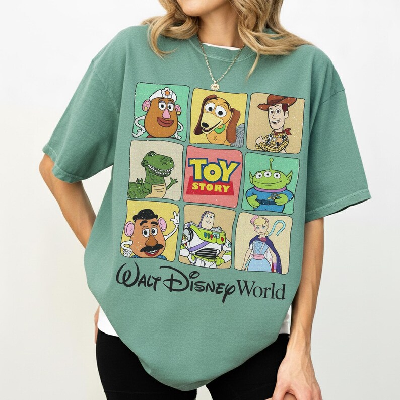 May include: A green t-shirt featuring a grid of Toy Story characters, including Woody, Buzz Lightyear, and Mr. Potato Head. The shirt has the words "Toy Story" and "Walt Disney World" printed on it.