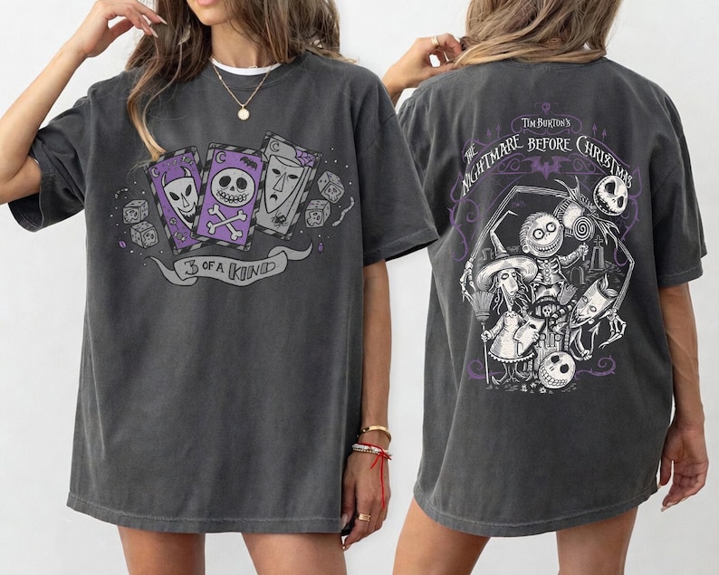 May include: Dark gray t-shirt featuring a graphic from Tim Burton's "The Nightmare Before Christmas." The front design shows three playing cards with skull faces and the text "3 of a Kind." The back displays a detailed scene with characters from the movie.