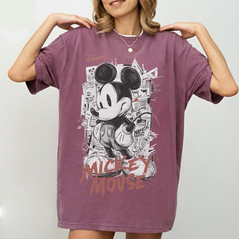 May include: A maroon t-shirt featuring a graphic of Mickey Mouse in a black and white urban style. The shirt has the text "Mickey Mouse" in a distressed font. The Disney logo is visible at the top left.