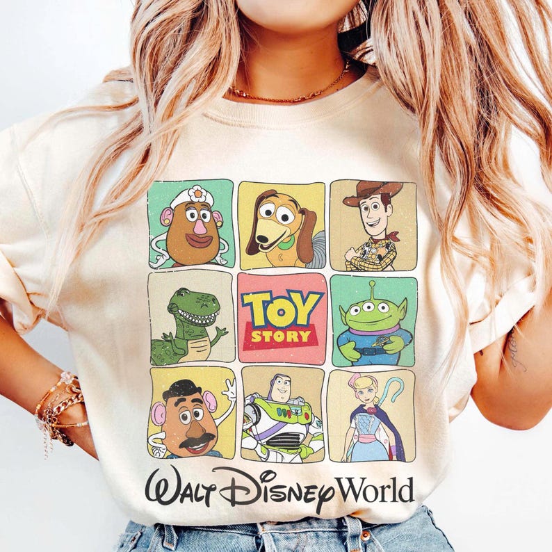 May include: Cream-colored t-shirt featuring a grid of Toy Story characters, including Mr. Potato Head, Slinky Dog, Woody, Rex, and Buzz Lightyear. The words "TOY STORY" are in the center, with "Walt Disney World" below.