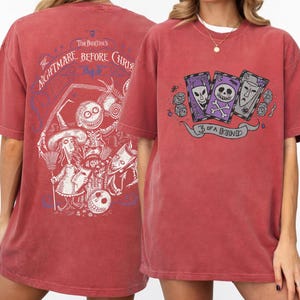 May include: Red-brown t-shirt featuring graphics from "The Nightmare Before Christmas." The front displays three playing cards with skull and alien designs, and the text "3 of a Kind." The back has a detailed character illustration.