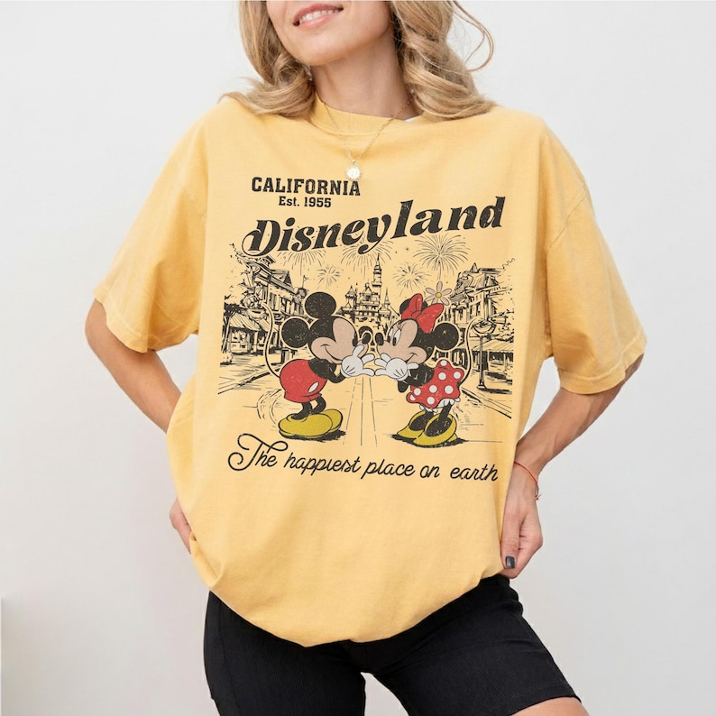May include: Yellow t-shirt with a Disneyland graphic featuring Mickey and Minnie Mouse. The graphic includes the text "CALIFORNIA Est. 1955 Disneyland" and "The happiest place on earth."
