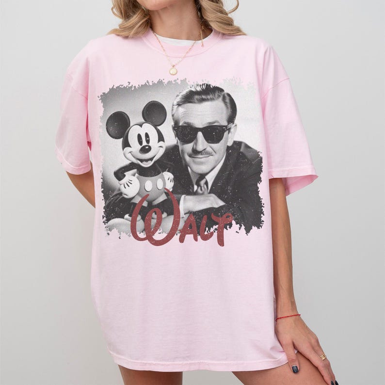 K&ouml;nnte beinhalten: Hellrosa T-Shirt mit einem Schwarz-Wei&szlig;-Bild von Walt Disney und Mickey Mouse. Das Wort "WALT" ist in roter Schrift darunter gedruckt. Das Shirt hat kurze &Auml;rmel und einen Rundhalsausschnitt.