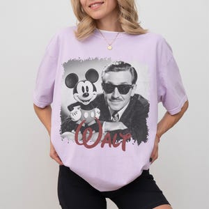 K&ouml;nnte beinhalten: Helllila T-Shirt mit einem Schwarz-Wei&szlig;-Bild von Walt Disney und Mickey Mouse. Das Wort "WALT" ist in roter Schrift gedruckt. Das T-Shirt ist im l&auml;ssigen Stil gehalten.