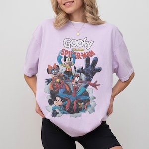 Op de afbeelding: Lichtpaars T-shirt met een stripboekafbeelding van Disney-personages als superhelden. De tekst "Goofy Became Spider-Man" staat boven de personages. Het shirt heeft korte mouwen.