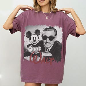 K&ouml;nnte beinhalten: Ein weinrotes T-Shirt mit einem Schwarz-Wei&szlig;-Motiv von Micky Maus und Walt Disney. Die Grafik hat einen Used-Look mit dem Namen "Walt" in Schreibschrift. Das Shirt hat kurze &Auml;rmel und einen Rundhalsausschnitt.