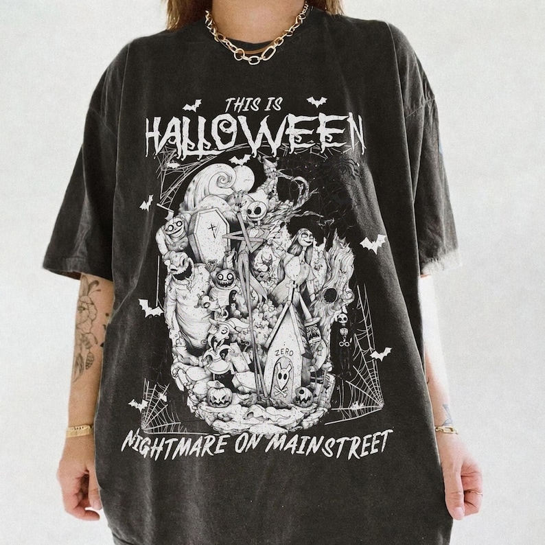 Puede incluir: Camiseta negra con un dise&ntilde;o gr&aacute;fico en blanco y negro inspirado en "Pesadilla antes de Navidad". El dise&ntilde;o incluye el texto "THIS IS HALLOWEEN" y "NIGHTMARE ON MAIN STREET", con murci&eacute;lagos y telara&ntilde;as.