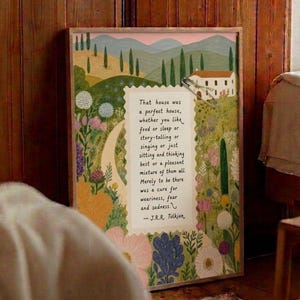 Puede incluir: Impresión artística enmarcada con un paisaje colorido, una casa y una cita de J.R.R. Tolkien. La obra de arte incluye un camino sinuoso, flores y árboles, con el texto: "That house was a perfect house..."