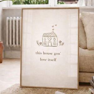 Könnte beinhalten: Gerahmter Kunstdruck mit einer minimalistischen Hausillustration und dem Text "this house gon' love itself". Das Kunstwerk zeigt eine einfache Strichzeichnung eines Hauses mit Herz und Rauch in einer neutralen Farbpalette.
