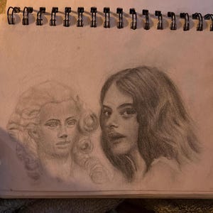 May include: Pencil sketch of two female faces in a spiral-bound sketchbook. One face is a historical figure with a powdered wig, and the other is a modern woman with long, wavy hair. The drawing is in shades of grey.