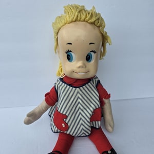May include: Vintage doll with a plastic head, blonde yarn hair, and blue eyes. The doll wears a red and white striped dress with red accents, red tights, and black shoes. A classic collectible toy.
