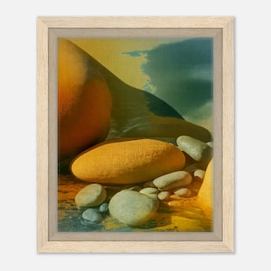 May include: Abstract art print in a light wood frame. The artwork features a composition of rounded, yellow-orange forms and smooth, gray stones, set against a backdrop of blended yellow, blue, and green hues, evoking a beach scene.