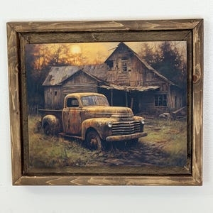 Puede incluir: Una impresión enmarcada representa una camioneta pickup amarilla oxidada y vintage estacionada frente a un granero de madera desgastado. La obra de arte presenta una puesta de sol y un paisaje rural, con una estética rústica y envejecida. El marco es de madera marrón oscuro.