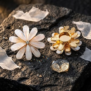 May include: Three floral-themed jewellery pieces. One is a white and gold flower-shaped brooch with a central crystal. Another is a gold-coloured setting with white accents. The third is a clear, round cabochon with gold leaf accents.