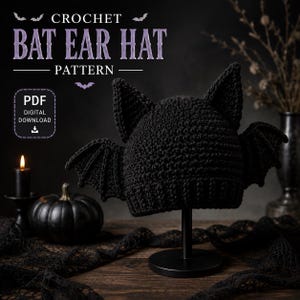 May include: A black crochet hat featuring two pointed bat ears on top and two bat wings attached to the sides. The text CROCHET BAT EAR HAT PATTERN PDF DIGITAL DOWNLOAD is visible in the upper portion of the image against a dark background.